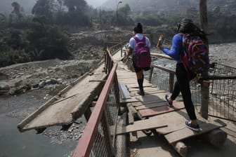 Menschen gehen über eine durch ein Hochwasser zerstörte Brücke in Peru (Archivbild).