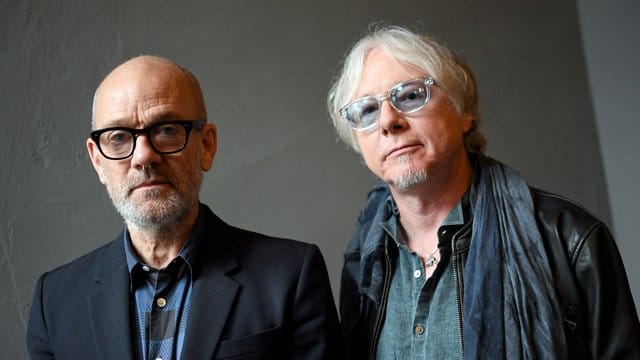 Mike Mills (r) und Michael Stipe stupsen sich gegenseitig an.