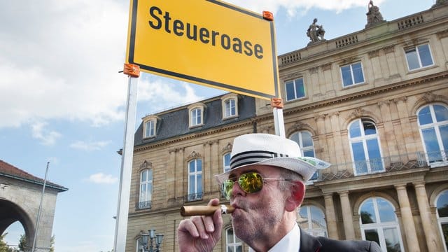 Ein Mann demonstriert auf dem Schlossplatz in Stuttgart vor einem Schild der Deutschen Steuer-Gewerkschaft mit der Aufschrift "Steueroase".