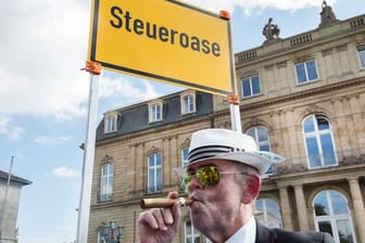 Ein Mann demonstriert auf dem Schlossplatz in Stuttgart vor einem Schild der Deutschen Steuer-Gewerkschaft mit der Aufschrift "Steueroase".