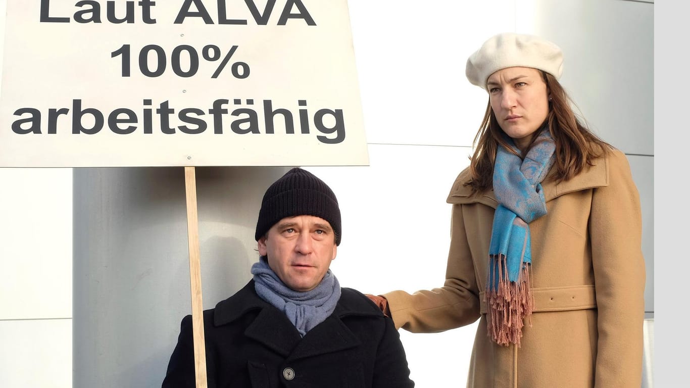 Harald Böhlert (Peter Schneider) und seine Frau Ines (Marie Leuenberger) demonstrieren vor der ALVA Versicherung. Rollstuhl, egal! Der Mann ist zu 100 Prozent arbeitsfähig.