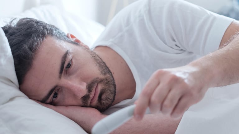 Kranker Mann liegt mit Fieberthermometer im Bett