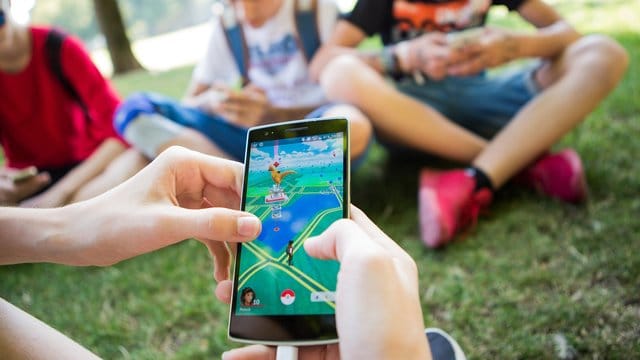 Jugendliche spielen in einem Park in Stuttgart auf ihren Smartphones.