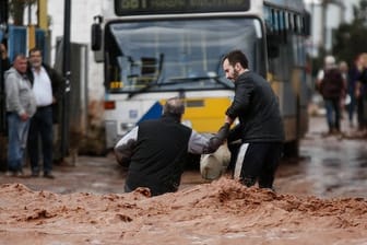 Ein Mann hilft an einer überflutete Straße in Mandra einem anderen Mann.