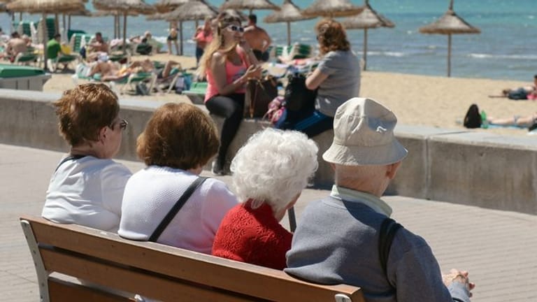 Senioren sitzen auf einer Bank an der Playa de Palma in S'Arenal bei Palma de Mallorca.