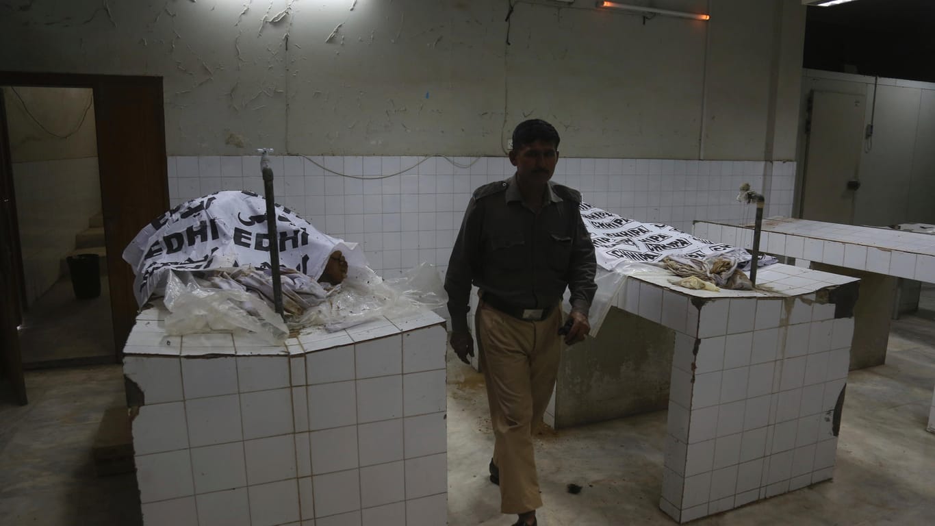 Ein pakistanischer Polizist geht an den Leichen vorbei, die auf zwei Tischen aufgebahrt sind. Mit Folien hat man das getötete Brautpaar provisorisch verhüllt.