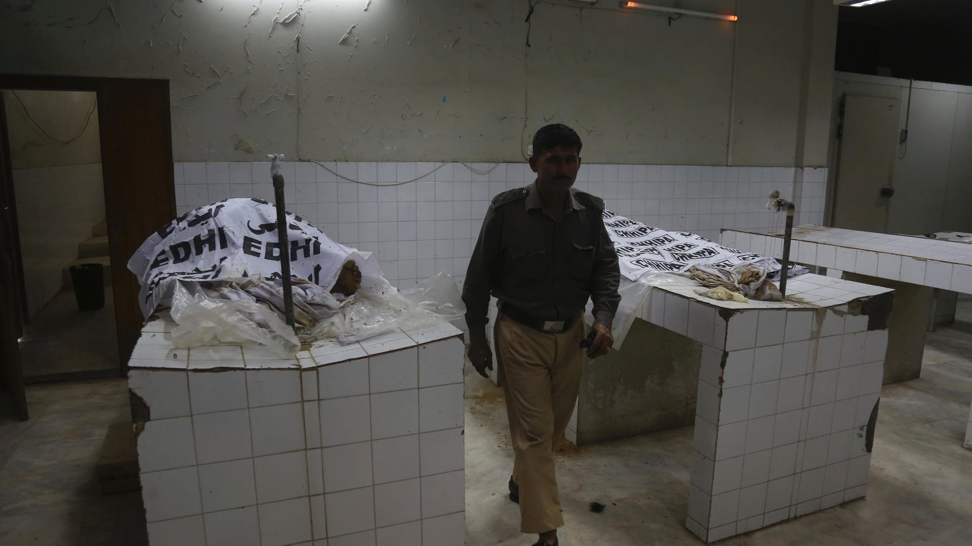 Ein pakistanischer Polizist geht an den Leichen vorbei, die auf zwei Tischen aufgebahrt sind. Mit Folien hat man das getötete Brautpaar provisorisch verhüllt. Ein pakistanischer Polizist geht an den Leichen vorbei, die auf zwei Tischen aufgebahrt sind. Mit Folien hat man das getötete Brautpaar provisorisch verhüllt.