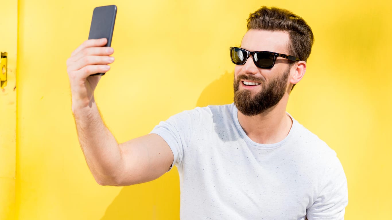 Ein Mann mit Bart und Sonnenbrille schießt ein Selfie.