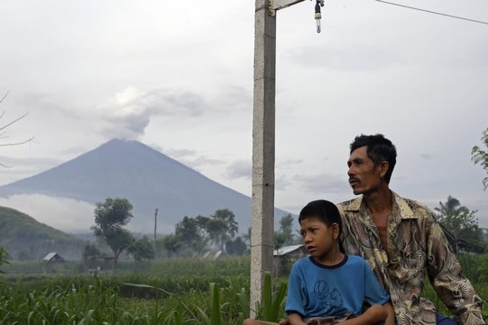 Ein Vater sitzt mit seinem Sohn vor der Kulisse des rauchenden Vulkans Mount Agung auf Bali.