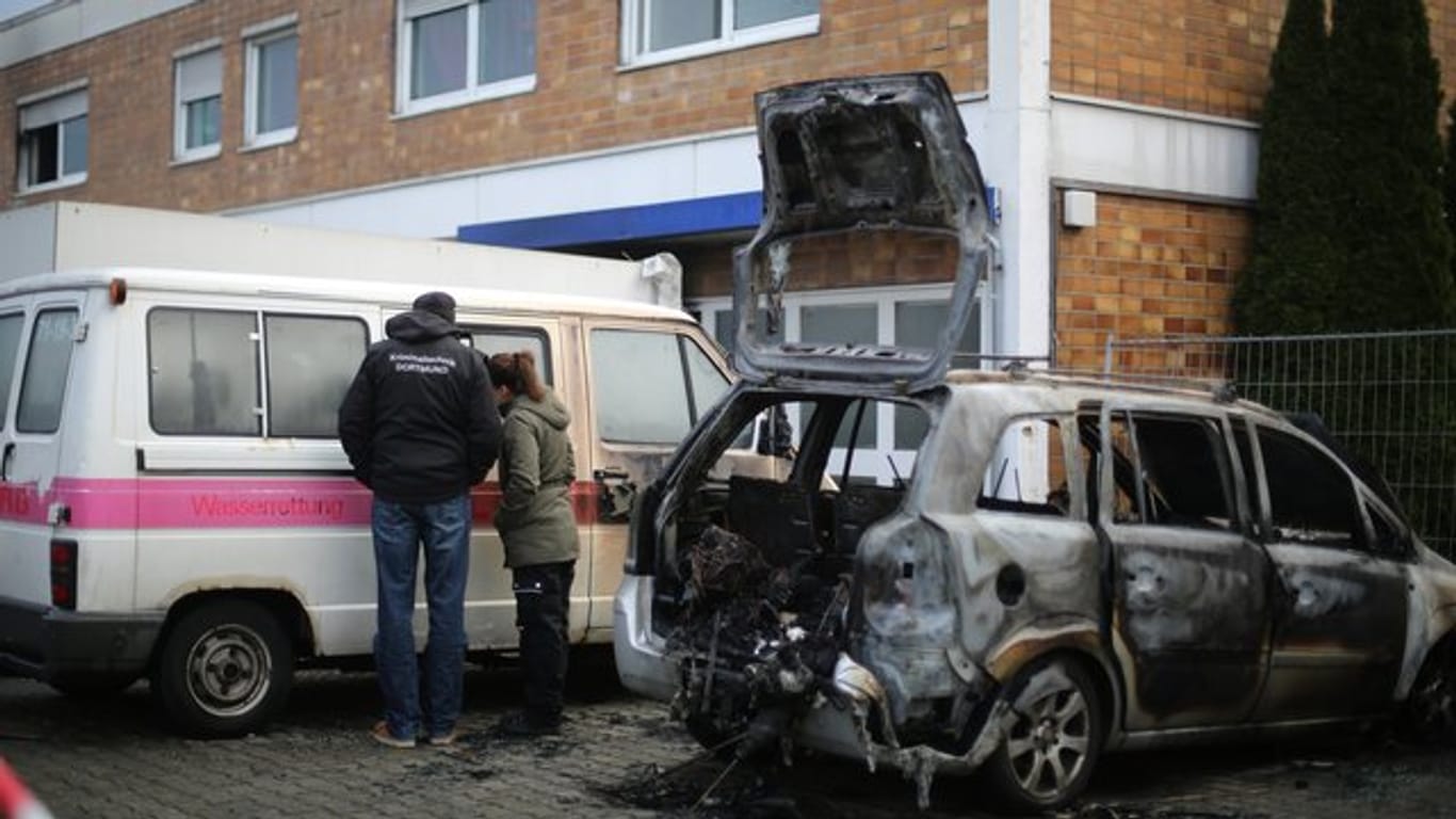 Kriminaltechniker begutachten in Bergkamen ein Auto vor einem Haus, in dem es in der Nacht gebrannt hat.