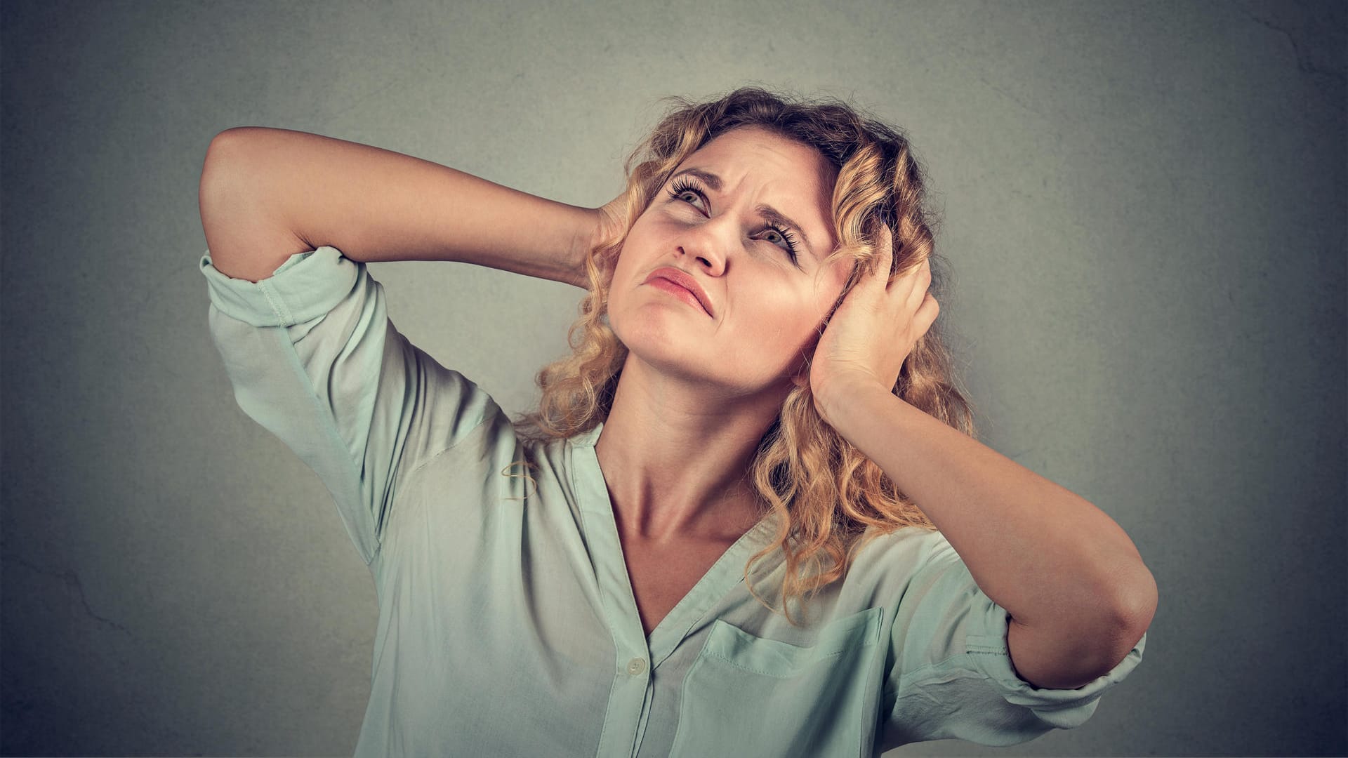 annoyed stressed woman covering ears with hands looking up