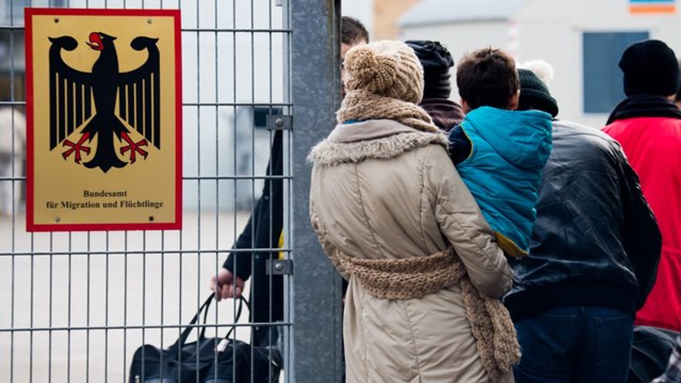 Flüchtlinge stehen neben einem Schild des Bundesamts für Migration und Flüchtlinge in Braunschweig.
