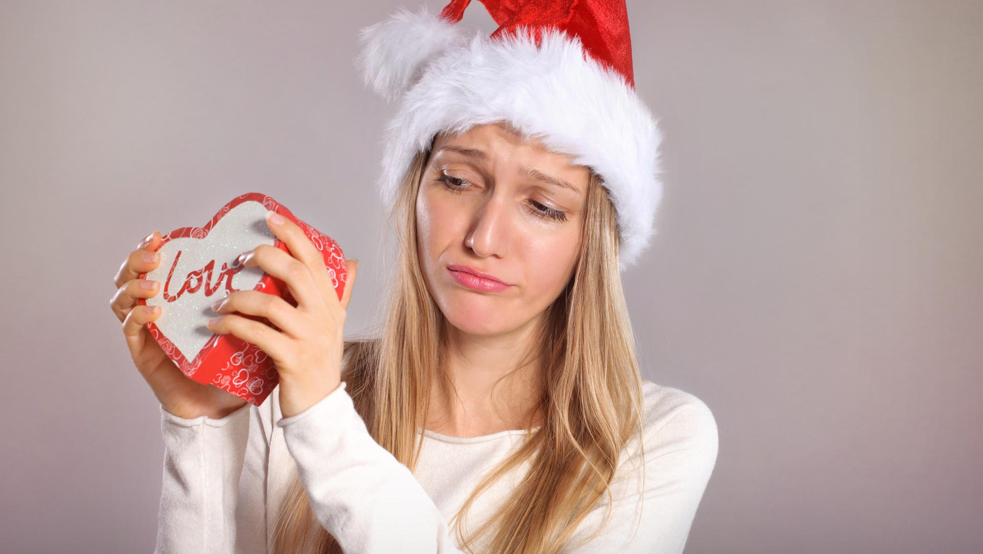 Disappointed woman with a Santa hat holding a gift box