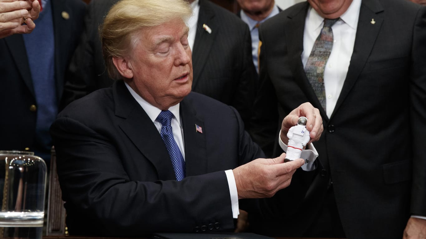 US-Präsident Donald Trump (M) hält im Roosevelt Room des Weißen Hauses in Washington (USA) eine Miniatur eines Astronauten, die ihm vom früheren Apollo-17-Astronauten Jack Schmitt (r) überreicht worden war: Die USA wollen die bemannte Raumfahrt zum Mond wieder aufnehmen.