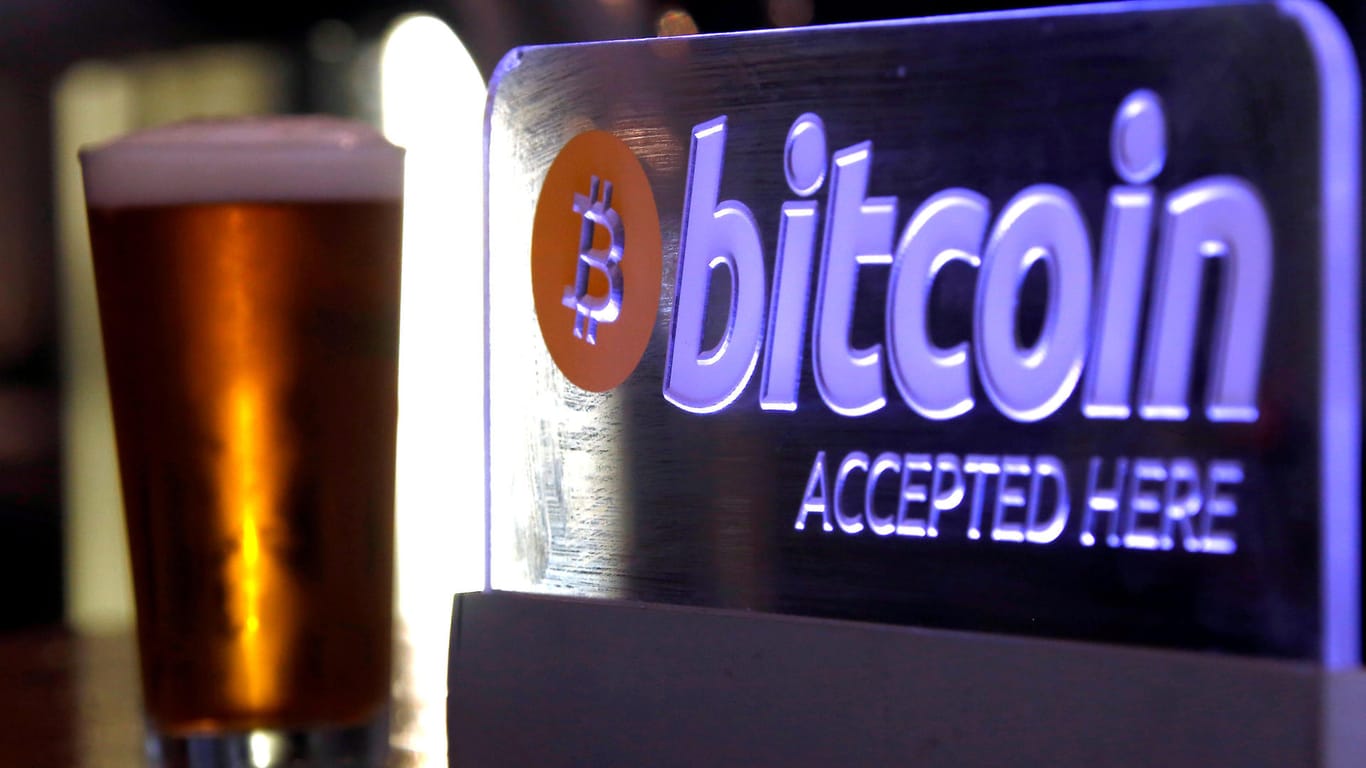 Ein Bierglas steht neben einem beleuchteten Logo von Bitcoin