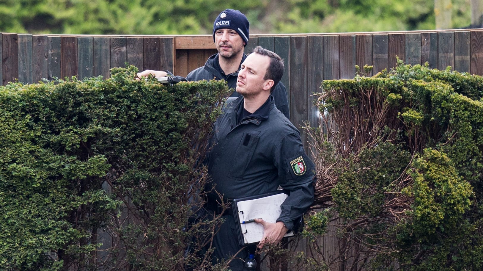 Ermittler der Polizei untersuchen in Dortmund Löcher in einer Hecke, wo die Sprengsätze explodiert sind.