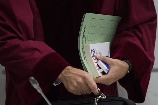 Ein Staatsanwalt beim Bundesgerichtshof hält Prozessunterlagen und ein Strafgesetzbuch in der Hand.