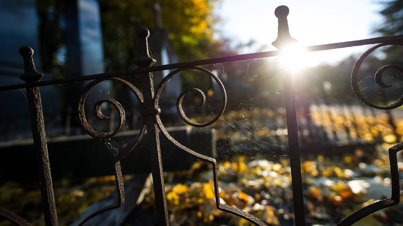 Ein rostiger Zaun begrenzt eine Grabfläche auf einem Friedhof.
