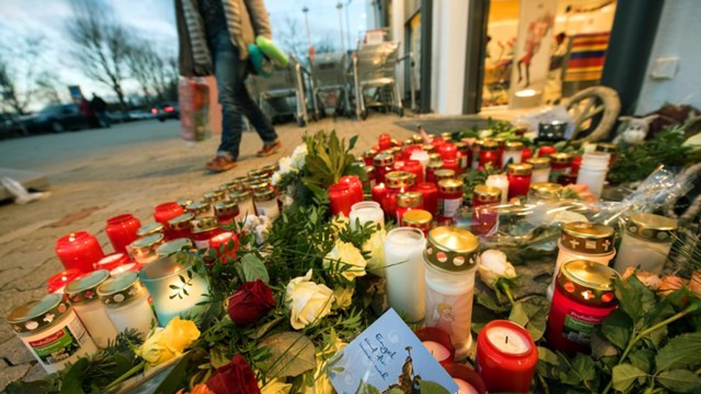 Ein Zettel mit der Aufschrift "Engel sind für immer nah" liegt vor dem Drogeriemarkt zwischen den abgelegten Blumen und Kerzen.