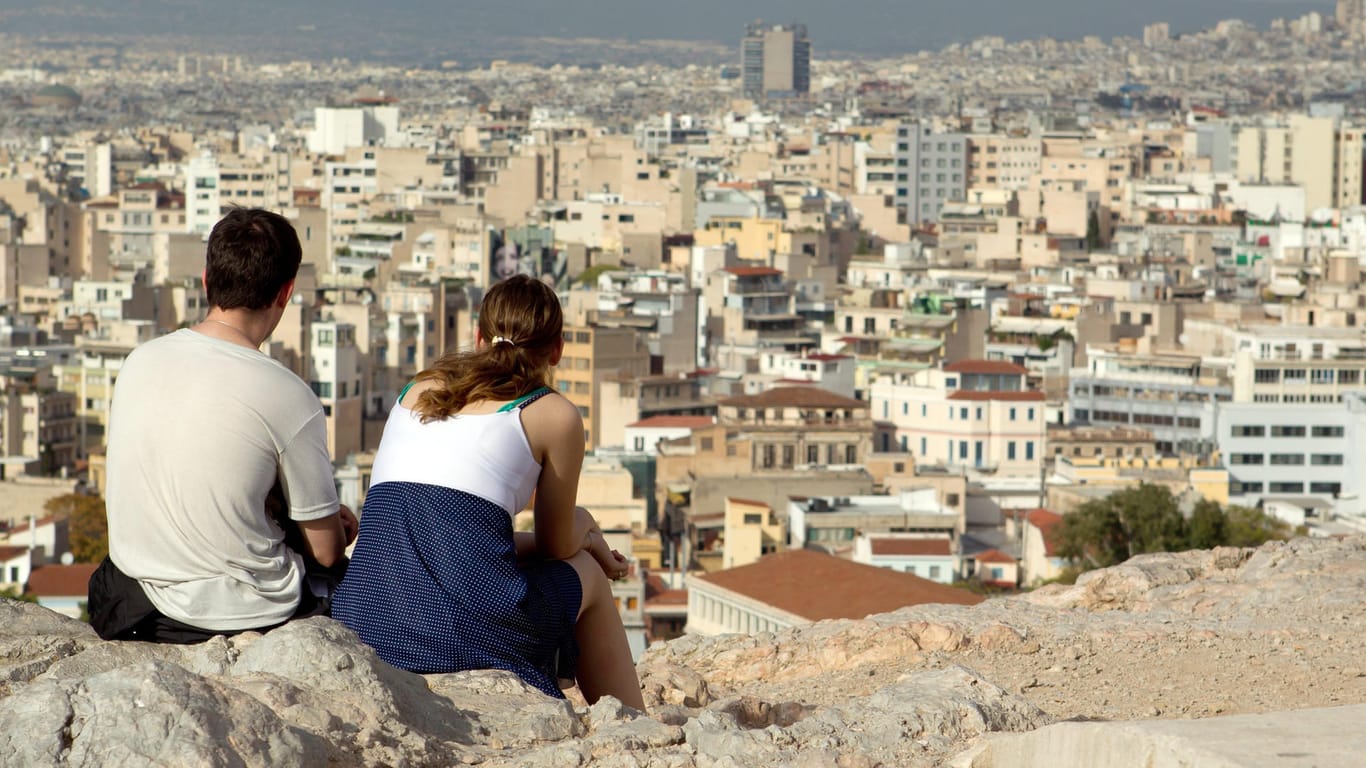 Ein junges Paar sitzt in Athen (Griechenland) auf einem Hügel und blickt über die Stadt: Griechenland ist aufgrund der Nähe ein beliebtes Ziel für viele Türken.