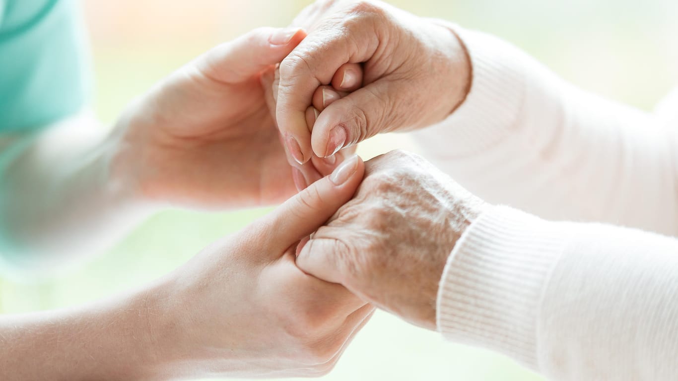 Pflegerin hält Hände einer älteren Frau