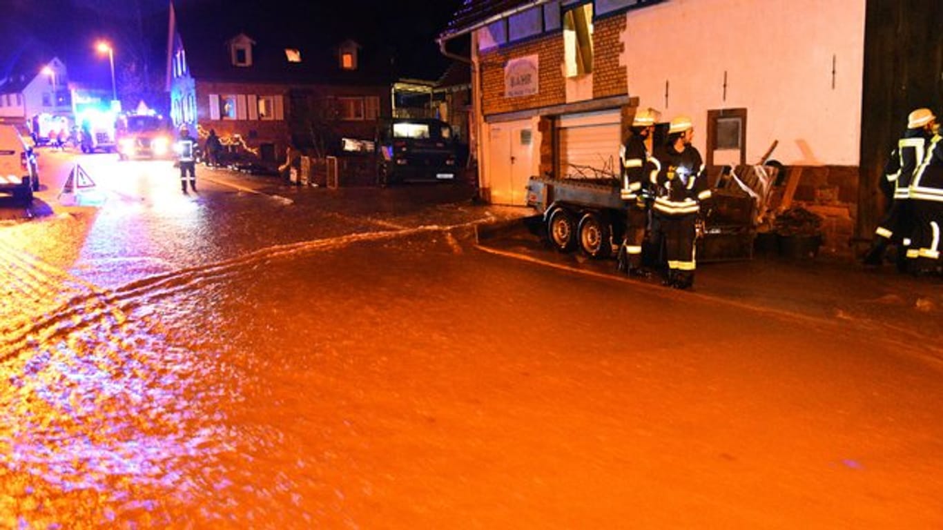Einsatzkräfte der Feuerwehr stehen in Waldhilsbach auf einer überfluteten Straße.