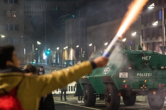 Ein Mann brennt in unmittelbarer Nähe eines gepanzerten Polizeifahrzeugs in Frankfurt am Main Feuerwerk ab.