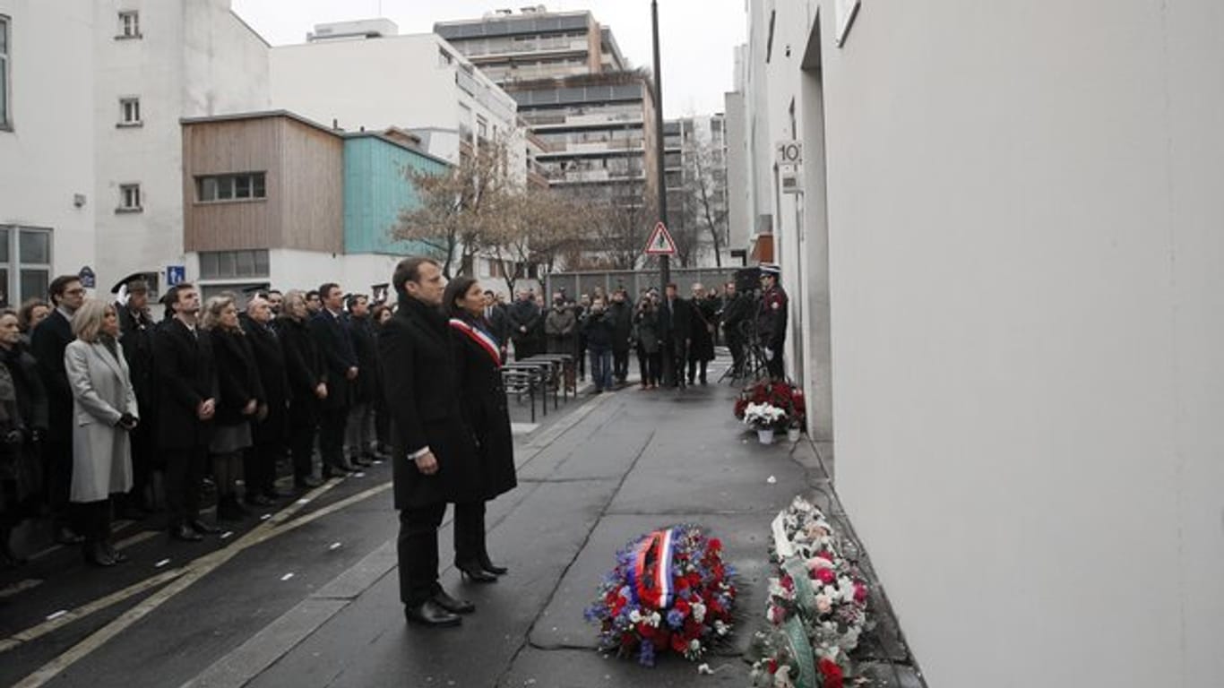 Der französische Präsident Emmanuel Macron und die Bürgermeisterin von Paris, Anne Hidalgo (Mitte, r), gedenken vor dem früheren Redaktionsgebäude des Satiremagazins "Charlie Hebdo" in Paris eine Schweigeminute der Opfer der islamistischen Anschlagsserie.