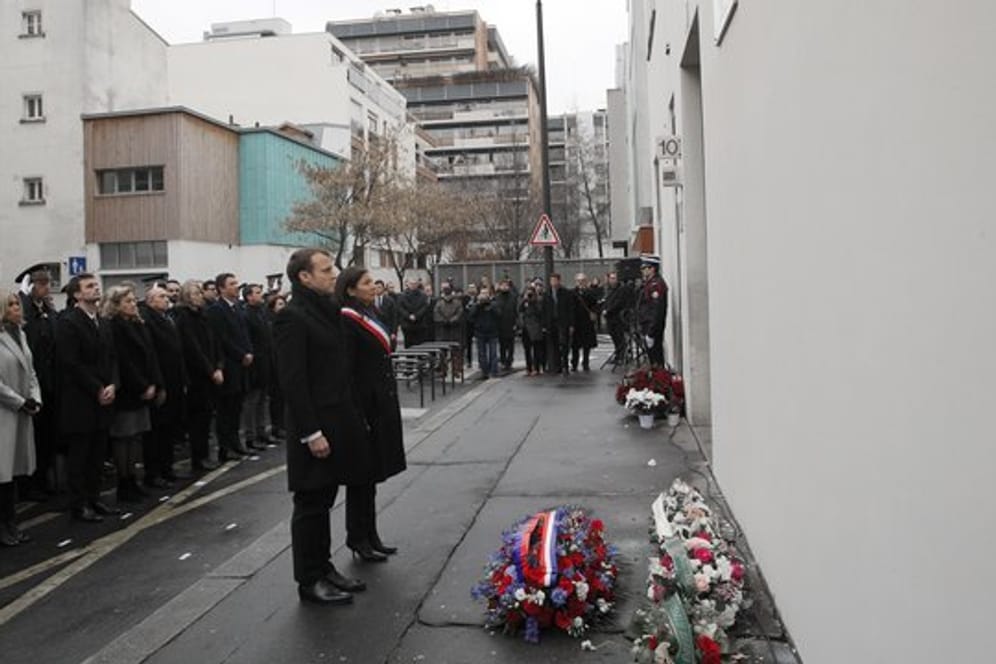 Der französische Präsident Emmanuel Macron und die Bürgermeisterin von Paris, Anne Hidalgo (Mitte, r), gedenken vor dem früheren Redaktionsgebäude des Satiremagazins "Charlie Hebdo" in Paris eine Schweigeminute der Opfer der islamistischen Anschlagsserie.