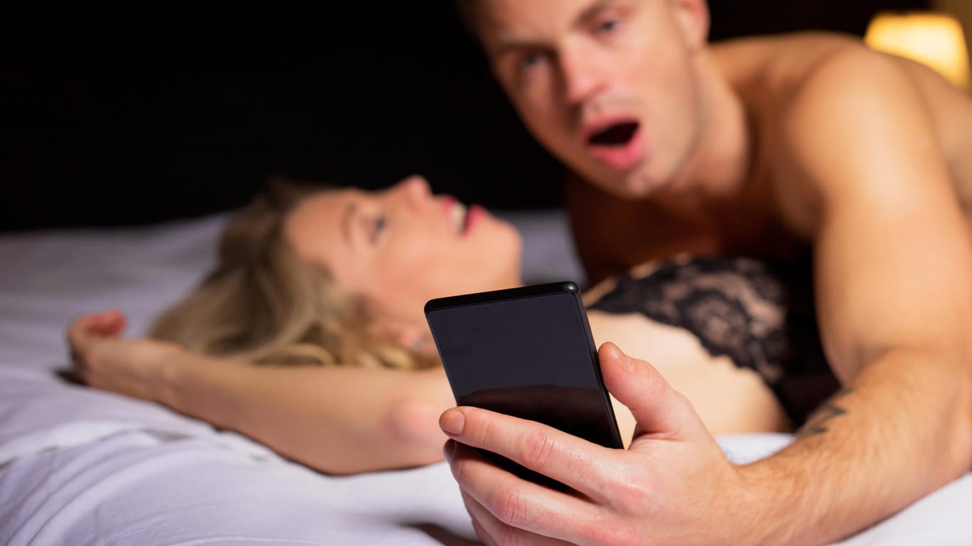 Mann schaut auf sein Handy beim Sex