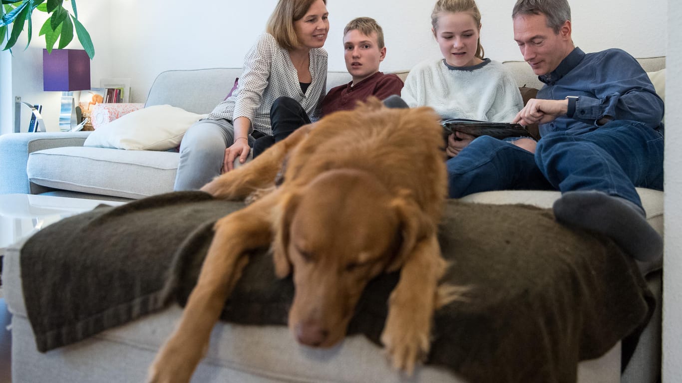 Katja Pleterski (l-r), Aron, der frühkindlichen Autismus hat, Helena und Niels Schumann sitzen hinter dem Autismusbegleithund Buddy auf der Couch.