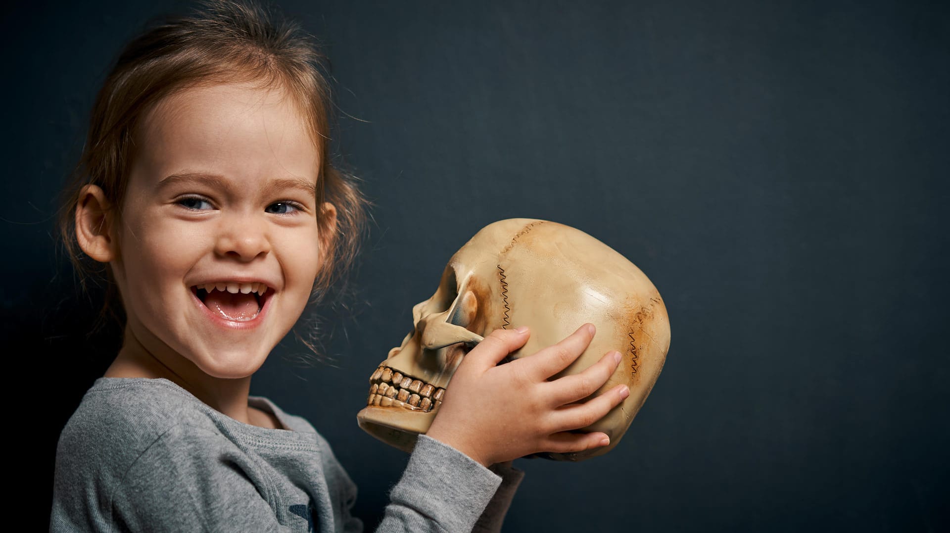 Niedliches Mädchen hält lachend einen Totenkopf fest