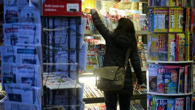 Eine Kundin sucht sich an einem Kiosk eine Zeitung aus.