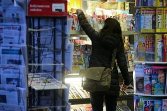 Eine Kundin sucht sich an einem Kiosk eine Zeitung aus.