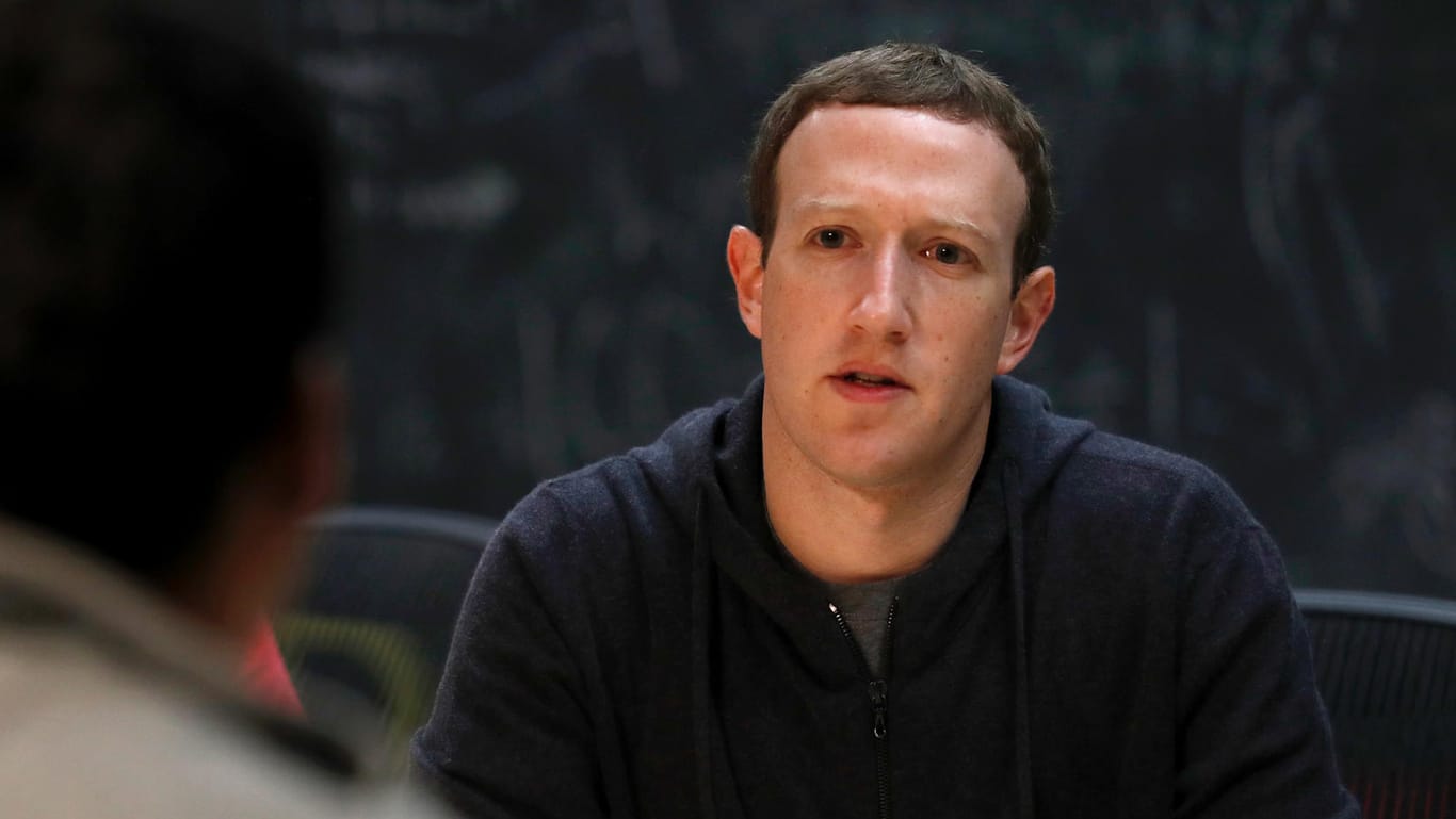 Facebook-Gründer Mark Zuckerberg: Nutzer vor Facebook-Logo: Nutzer des Netzwerks sollen über die Qualität von zitierten Medien entscheiden.