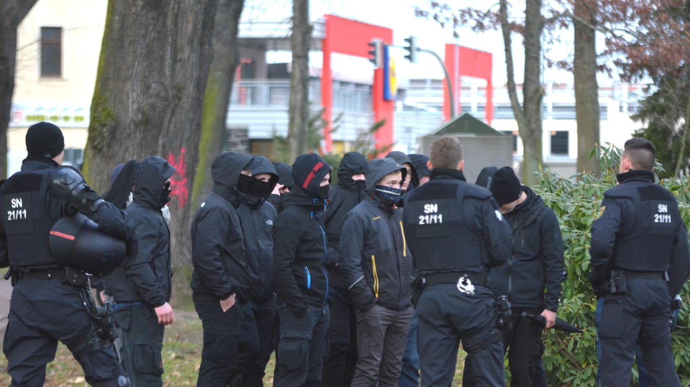 Vermummte Neonazis stehen neben Polizisten. Laut der sächsischen Polizei mussten die Rechten die Vermummungen abnehmen, um zu ihrer eigenen Demonstration zu gelangen.