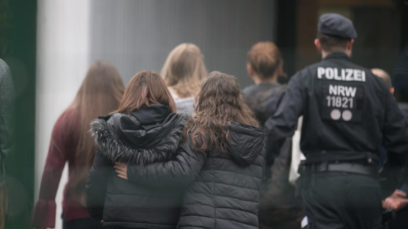 Polizisten begleiten Kinder über den Pausenhof der Käthe Kollwitz Gesamtschule: Ein Schüler soll von einem Mitschüler getötet worden sein. Ein minderjähriger Tatverdächtiger wurde im Rahmen einer Fahndung festgenommen.