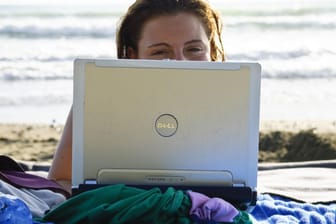 Eine Frau liegt mit ihrem Laptop am Strand
