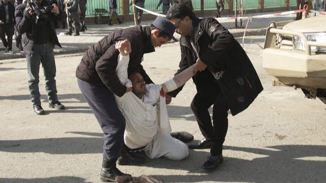 Zwei Männer helfen in Kabul nach einem Anschlag einem verwundeten Mann.