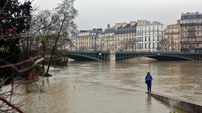 Eine Frau an der Seine in Paris. Das Hochwasser ist über das Flussufer getreten.