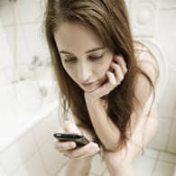 Frau mit Handy auf Toilette: Smartphones werden schnell zur "Bakterienfalle".