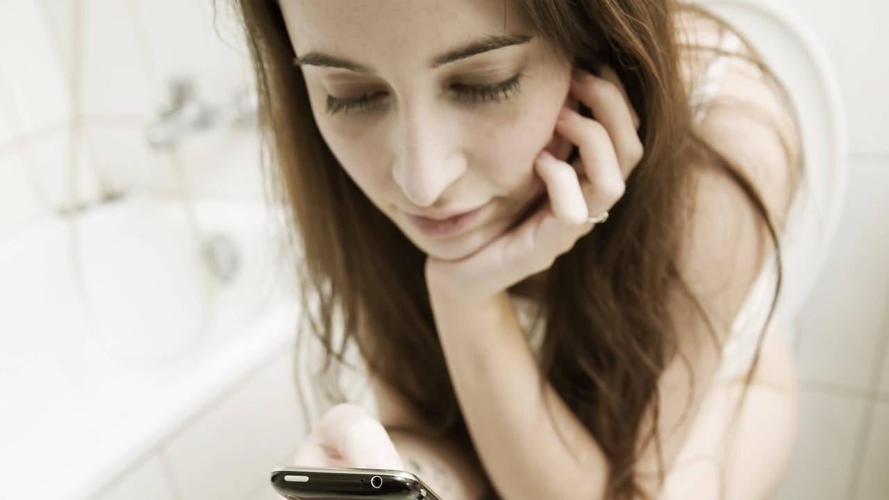 Frau mit Handy auf Toilette: Smartphones werden schnell zur "Bakterienfalle".