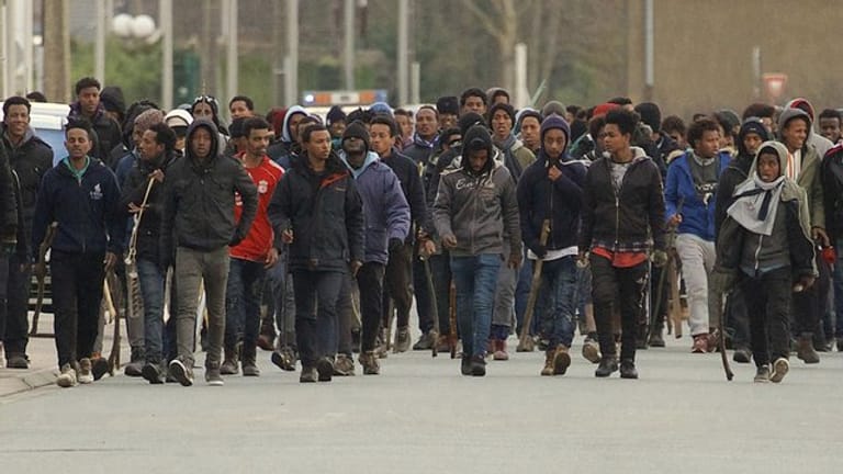 Flüchtlinge mit Stöcke marschieren durch die Straßen von Calais.