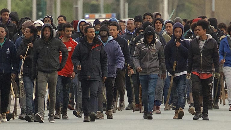Flüchtlinge tragen Stöcke und marschieren durch die Straßen von Calais (Frankreich): Bei Auseinandersetzungen zwischen Migranten im nordfranzösischen Calais sind vier Menschen durch Schüsse lebensgefährlich verletzt worden.