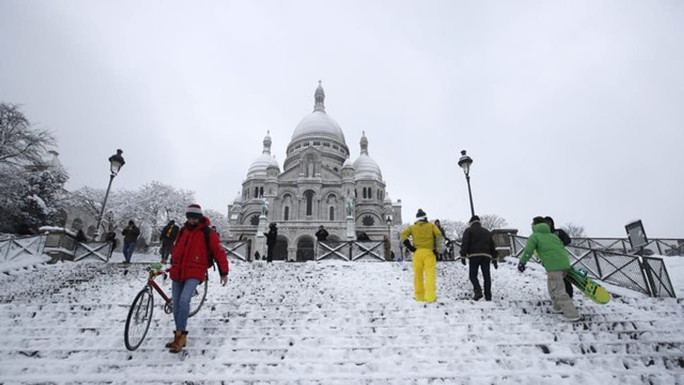 Menschen gehen über die verschneite Treppe auf den Montmatre mit der Basilika Sacre Coeur.