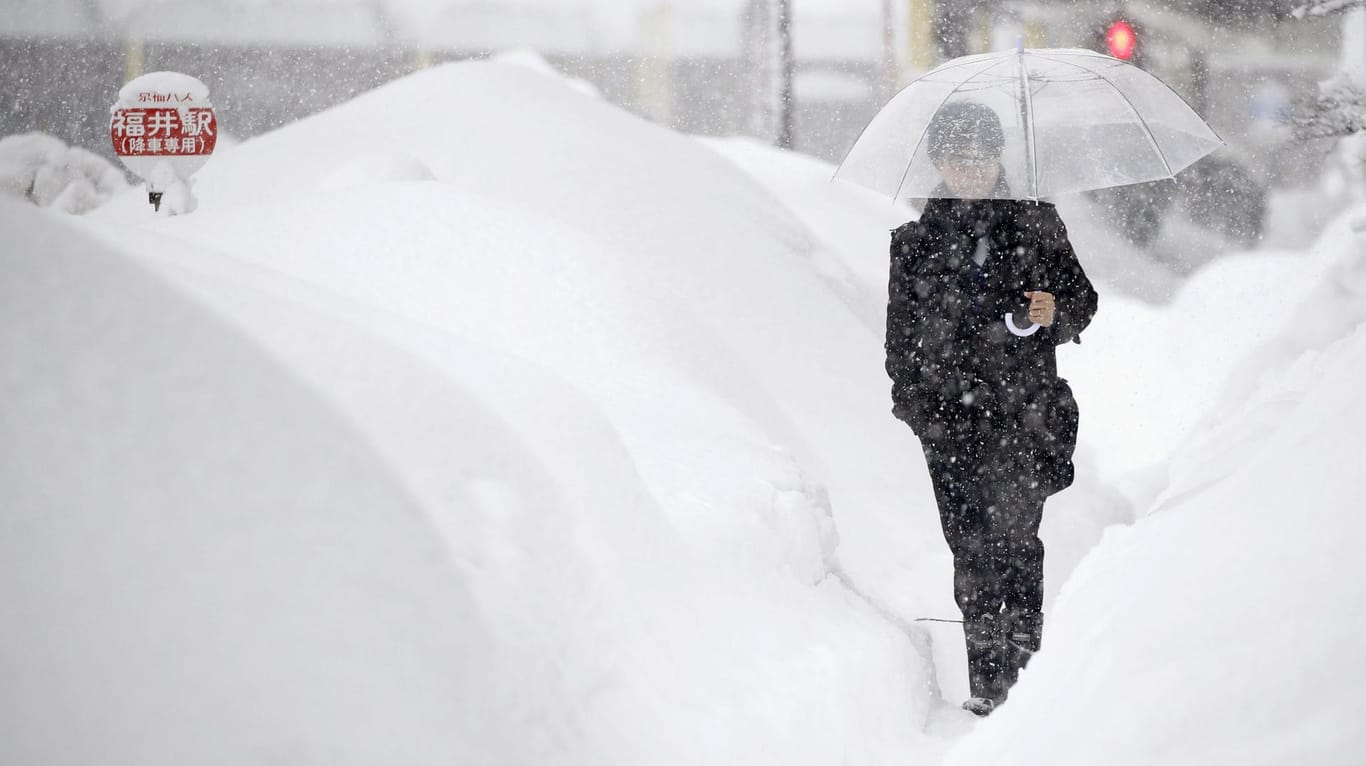 Person läuft auf einer stark verschneiten Straße Fukui (Japan) entlang: Mehrere hundert Autos stecken in Schneemassen in Japan fest.