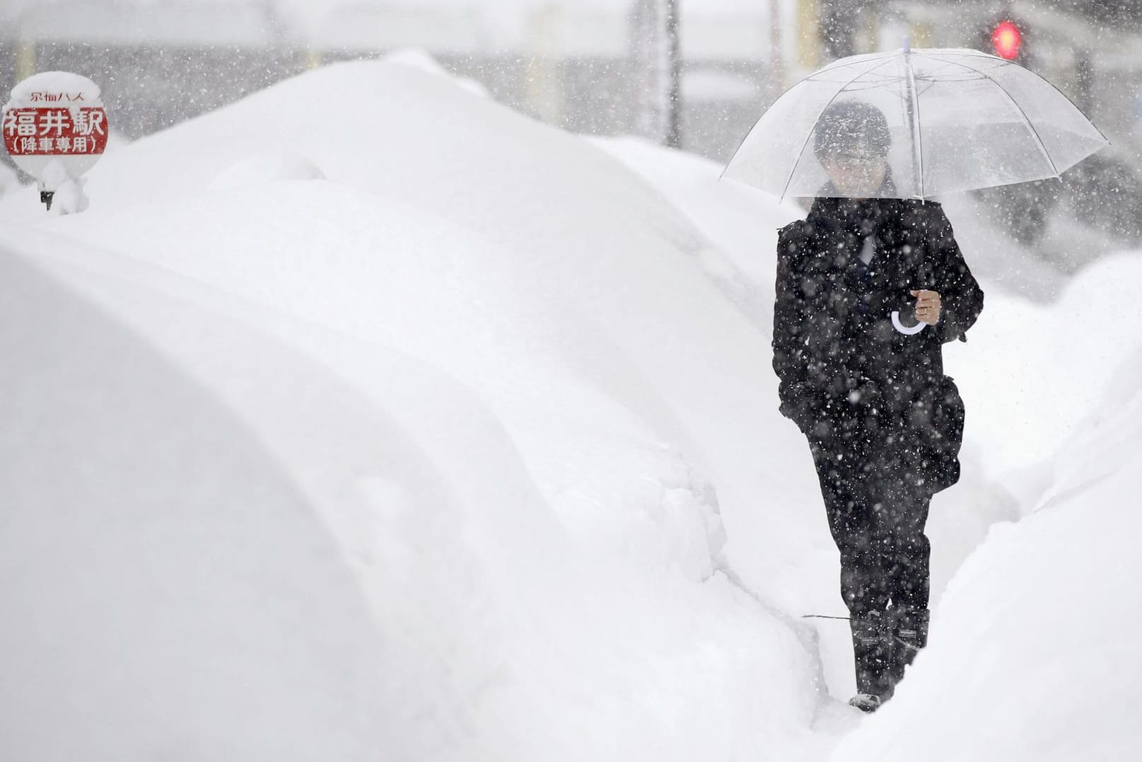 Person läuft auf einer stark verschneiten Straße Fukui (Japan) entlang: Mehrere hundert Autos stecken in Schneemassen in Japan fest.