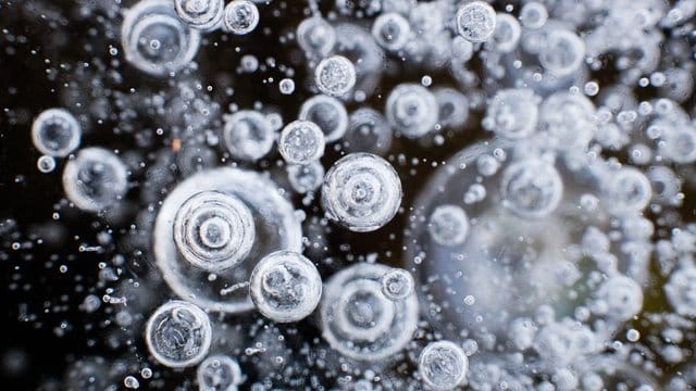Luftblasen sind im Eis einer zugefrorenen Wasserfläche zu sehen. Luftblasen sind im Eis einer zugefrorenen Wasserfläche zu sehen.