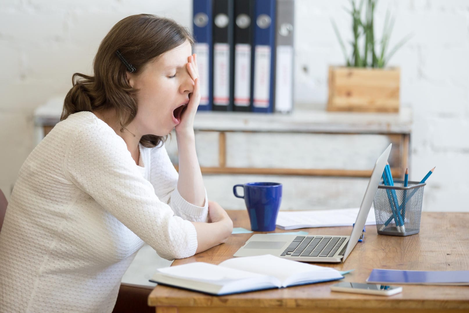 Müde Frau am Arbeitsplatz: Fehlt dem Körper frische Luft, weil man den Großteil des Tages in schlecht gelüfteten Räumen sitzt, raubt das Energie und verstärkt die Müdigkeit.