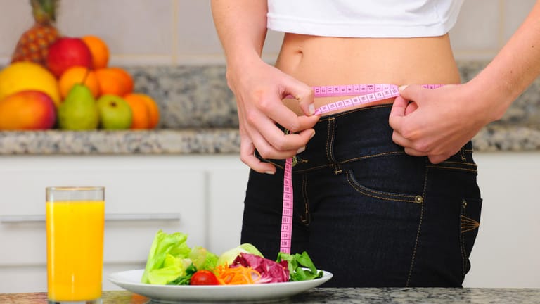 Eine schlanke Frau misst ihren Bauchumfang: Beeinflussen genetisch festgelegte Stoffwechseleigenschaften, wie gut jemand auf eine bestimmte Diät anspricht?